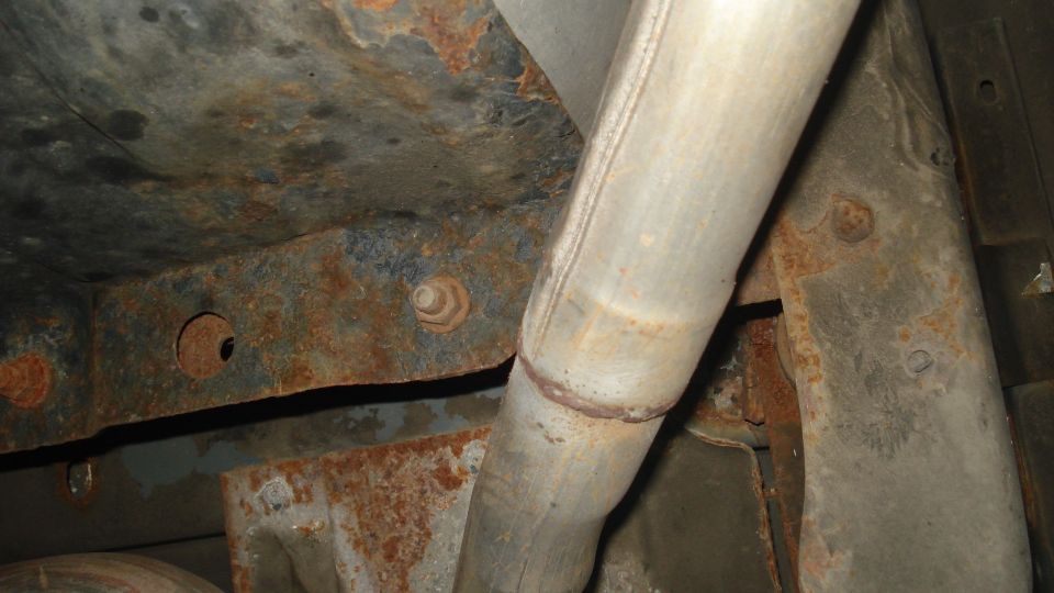 Underside of a vehicle showing rusted frame and exhaust pipe