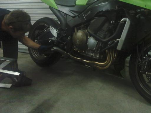 Man working on motorcycle exhaust pipes and engine. Green bodywork visible