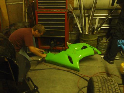 Green motorcycle fairing on floor, man working on it