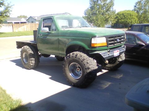 1989 Ford Bronco - This lifted green flatbed truck features aggressive off-road tires and a modified front end.