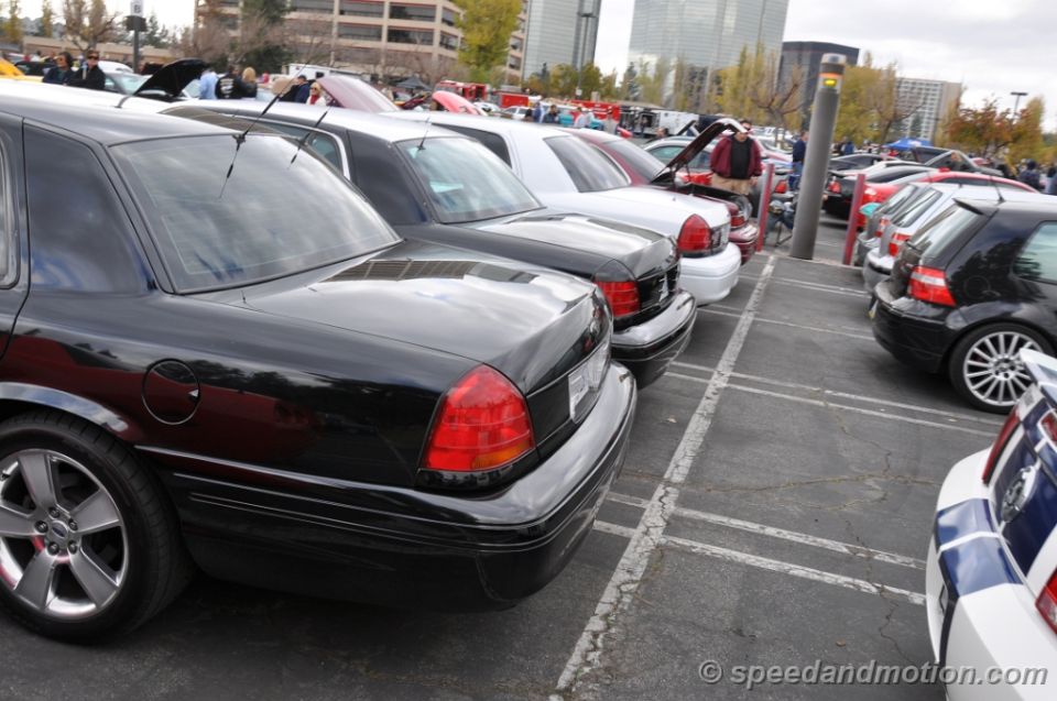 Black Ford Crown Victoria parked in a lot with other cars. Rear view shows taillights and trunk