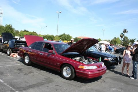 1992 Ford Crown Victoria - A red 1992 Ford Crown Victoria sedan is parked with its hood open, alongside other vehicles.