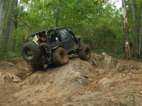 1996 Ford Bronco - An off-road vehicle navigates a challenging rocky trail in a wooded area.