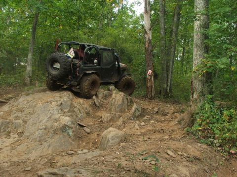 1996 Ford Bronco - Off-road vehicle navigating a challenging rocky path through a wooded area.