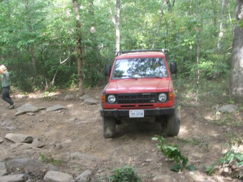 1996 Ford Bronco - This red Mitsubishi Pajero is navigating a rocky trail in a wooded area.