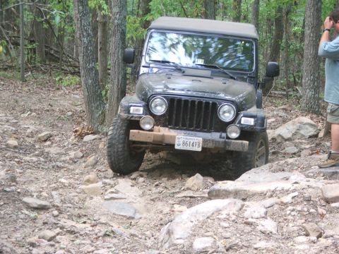 1996 Ford Bronco - A black Jeep Wrangler tackles a challenging rocky path, demonstrating its off-road capabilities.