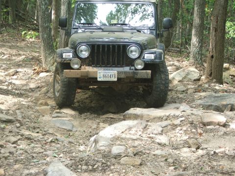 1996 Ford Bronco - Jeep Wrangler TJ navigating a challenging rocky trail in a wooded area.