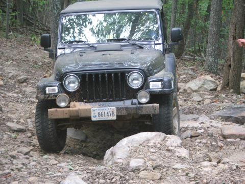 1996 Ford Bronco - A Jeep Wrangler Rubicon navigates a challenging, rocky off-road path surrounded by trees.