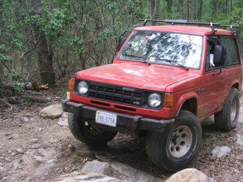 1996 Ford Bronco - This red Mitsubishi Montero is navigating a challenging rocky trail in a wooded area.