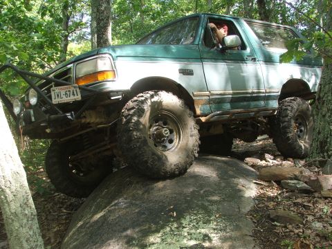 1996 Ford Bronco - A modified green Ford Bronco navigates a rocky trail in a wooded area.