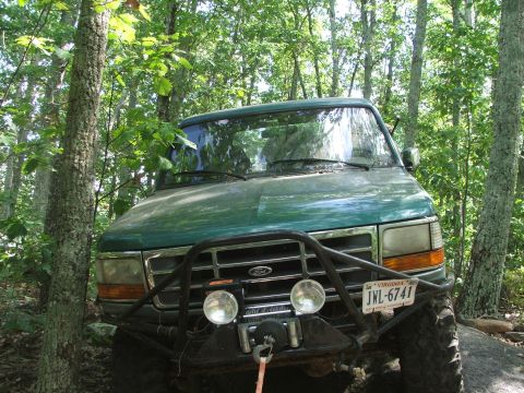 1996 Ford Bronco - This Ford Bronco is parked off-road in a wooded area, a custom front bumper with a winch and auxiliary lights.