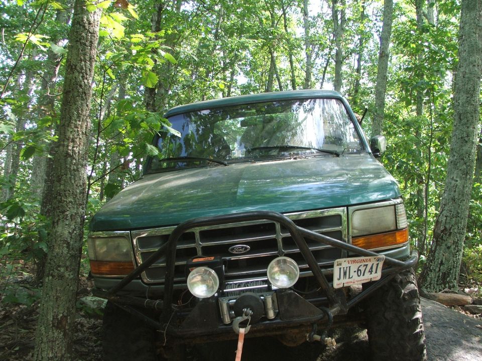 Green Ford Bronco with a winch and brush guard parked in woods. License plate JWL-6741