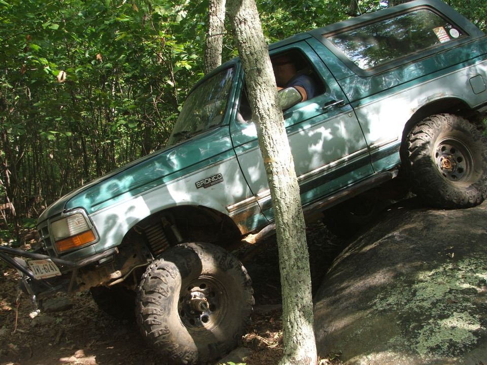 Green 1996 Ford Bronco navigating a large rock on a trail
