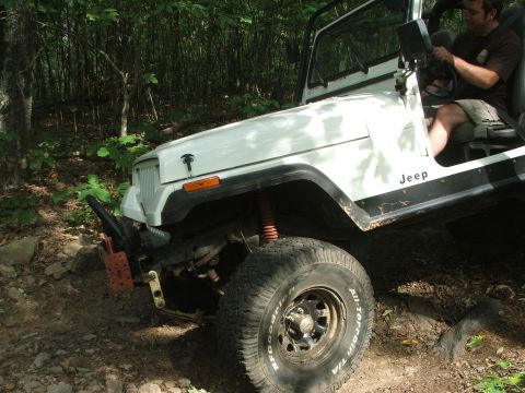 1996 Ford Bronco - White Jeep Wrangler navigating an off-road trail with a driver at the wheel.