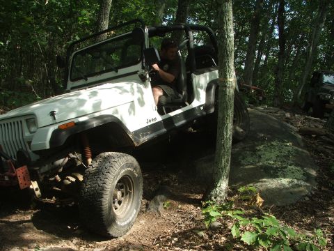1996 Ford Bronco - A white Jeep navigates a rocky trail in a wooded area, with another vehicle following behind.