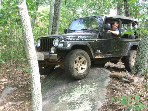 1996 Ford Bronco - A black Jeep Wrangler Rubicon navigates a rocky trail in a wooded area.