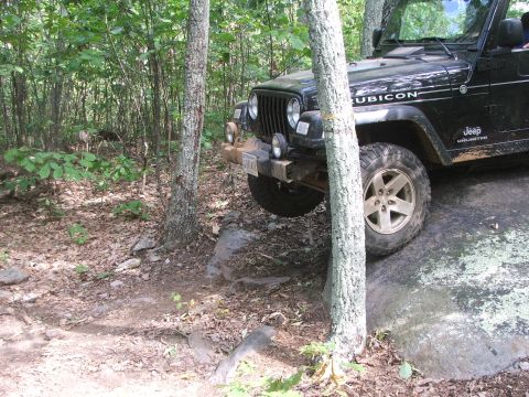 1996 Ford Bronco - A black Jeep Wrangler Rubicon tackles a challenging rocky trail, with its tires positioned on large boulders.