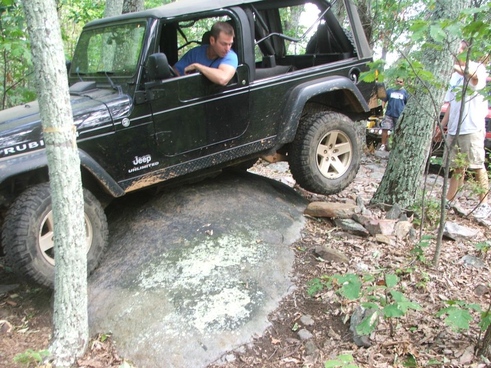 Black Jeep Wrangler with "Rubicon" and "Jeep Unlimited" decals on its side, navigating over a large rock off-road