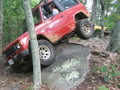 1996 Ford Bronco - This red off-road SUV navigates a challenging rocky trail, with another Jeep visible in the background.
