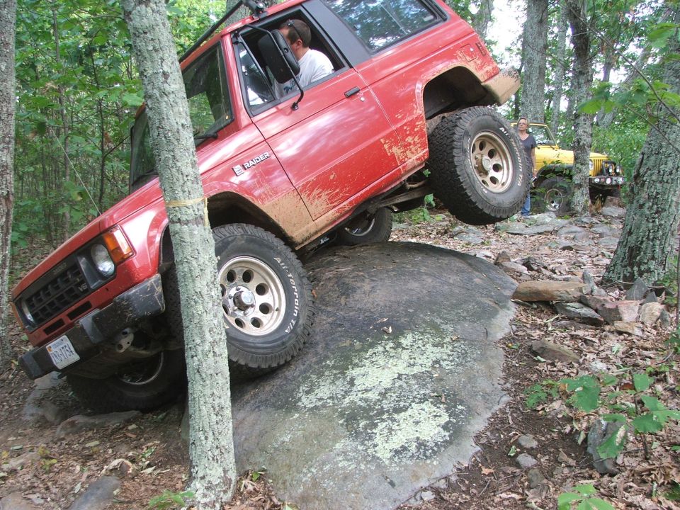 Red off-road SUV with 'Raider' badge climbing over a rock, yellow Jeep in background