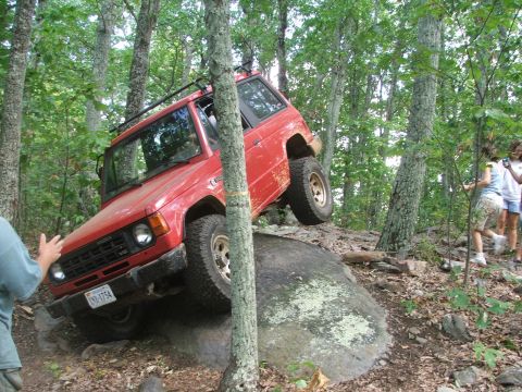 1996 Ford Bronco - A red SUV attempts to climb over a large rock on a challenging off-road trail.