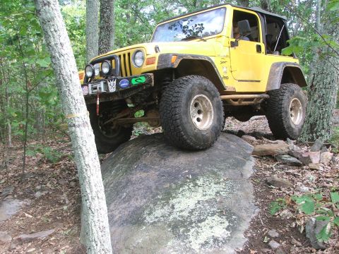 1996 Ford Bronco - A yellow Jeep Wrangler navigates a challenging rocky obstacle on an off-road trail.