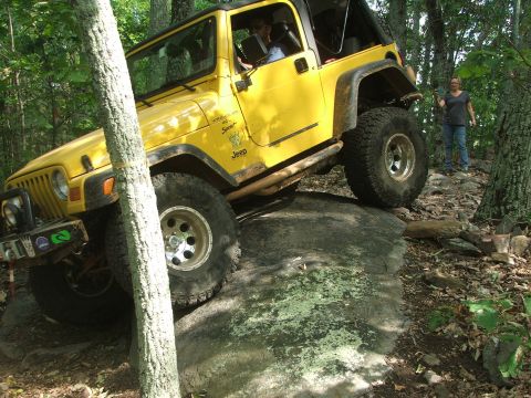 1996 Ford Bronco - Yellow Jeep Wrangler TJ navigating a rocky trail in the woods.