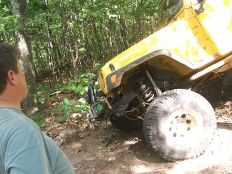 1996 Ford Bronco - A person looks at a yellow off-road vehicle on a wooded trail.