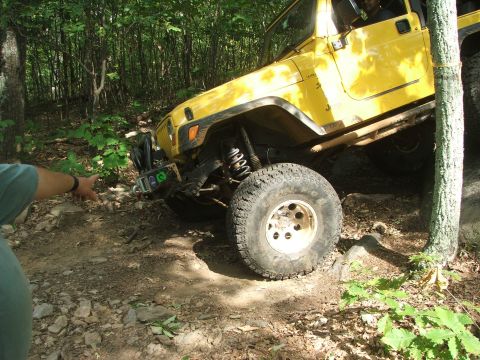 1996 Ford Bronco - A yellow Jeep Wrangler navigates a rocky, wooded trail during an off-road excursion.