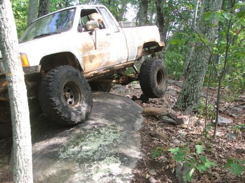 1996 Ford Bronco - This modified pickup truck is navigating a difficult off-road course through a forest.