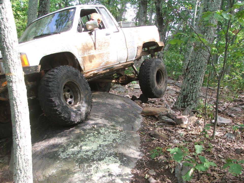 White pickup truck with large tires climbing over rocks on a wooded trail