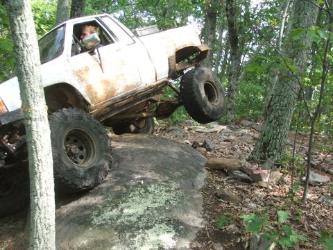 1996 Ford Bronco - A white off-road truck navigates a rocky trail with one wheel lifted off the ground.