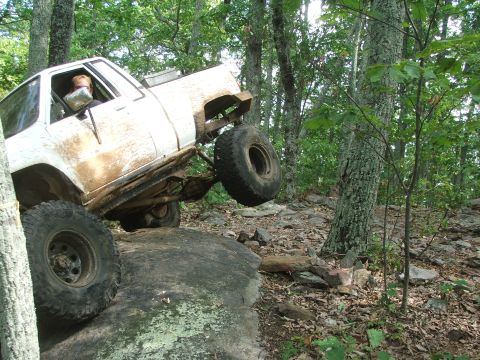 1996 Ford Bronco - This white SUV is navigating a challenging rocky terrain, with one wheel lifted high off the ground.