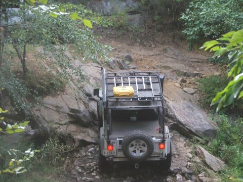 1996 Ford Bronco - Off-roading Jeep Wrangler navigates a challenging rocky path through a wooded area.