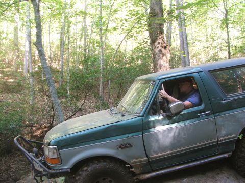1996 Ford Bronco - A green and grey Ford Bronco navigates a wooded trail, its driver visible behind the wheel.