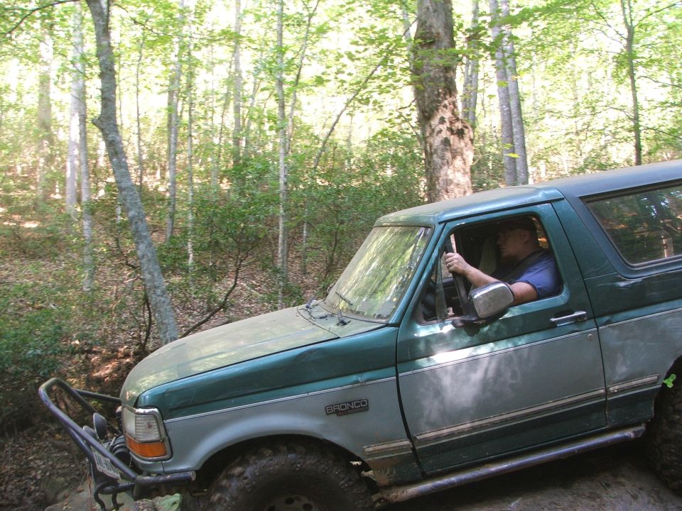 Green and grey Ford Bronco off-roading, front fender visible with "BRONCO" badge