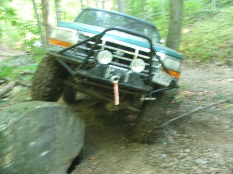 1996 Ford Bronco - This modified Ford Bronco is navigating a challenging off-road course with large rocks and trees.