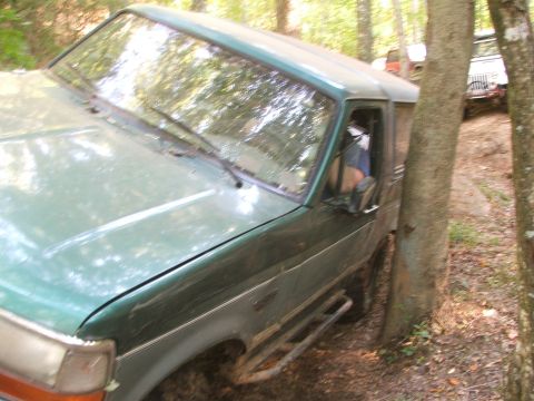 1996 Ford Bronco - A green 1996 Ford Bronco navigates a wooded trail, with another vehicle visible in the background.