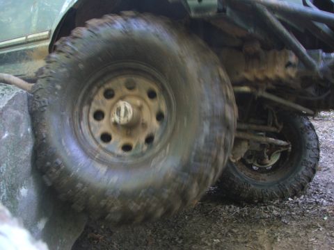 1996 Ford Bronco - A vehicle's tire is shown navigating a rocky obstacle, with mud and dirt visible on the undercarriage.