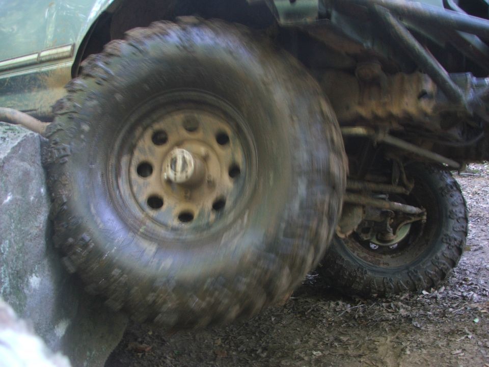 close-up of a muddy off-road tire climbing over a large rock