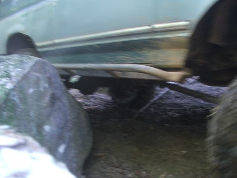 1996 Ford Bronco - A side view of a vehicle's undercarriage, showing its frame and exhaust system on a muddy ground.