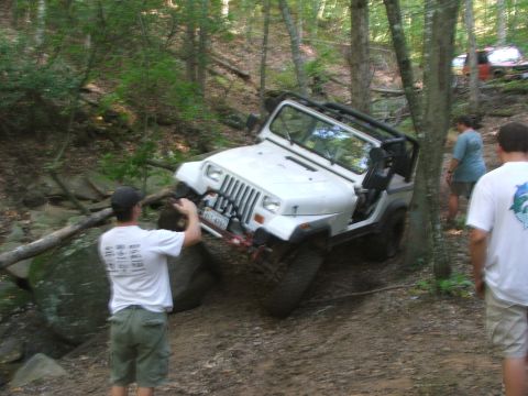 1996 Ford Bronco - A white Jeep Wrangler navigates a rocky off-road trail with two onlookers present.