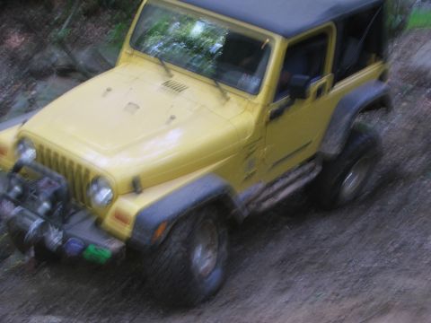 1996 Ford Bronco - Yellow Jeep Wrangler navigating an off-road trail with large tires.