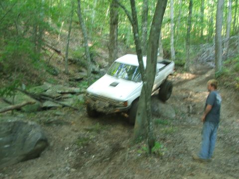 1996 Ford Bronco - A white pickup truck navigates a challenging off-road trail through a dense forest.