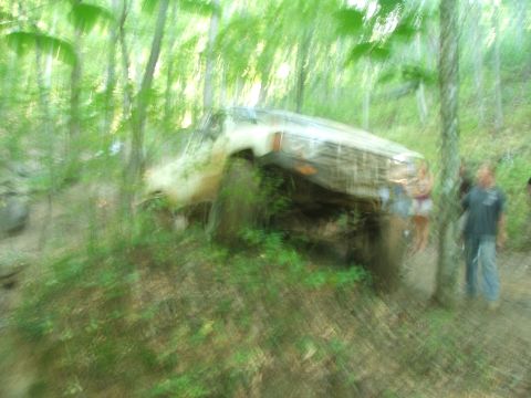 1996 Ford Bronco - An off-road vehicle is tilted on a hill in a wooded area, with two people standing nearby.