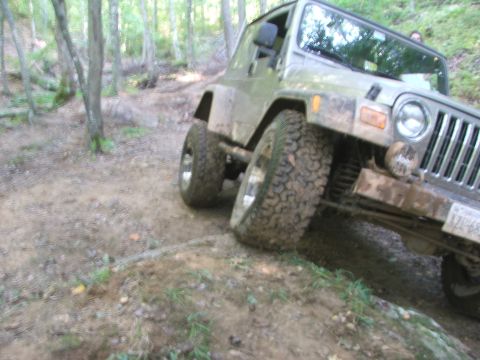 1996 Ford Bronco - A silver Jeep Wrangler TJ navigates a muddy, wooded trail.