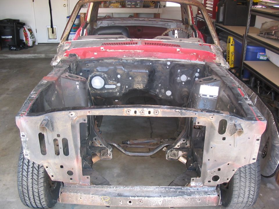 Red car chassis, front view, missing engine and body panels, showing rust and wear