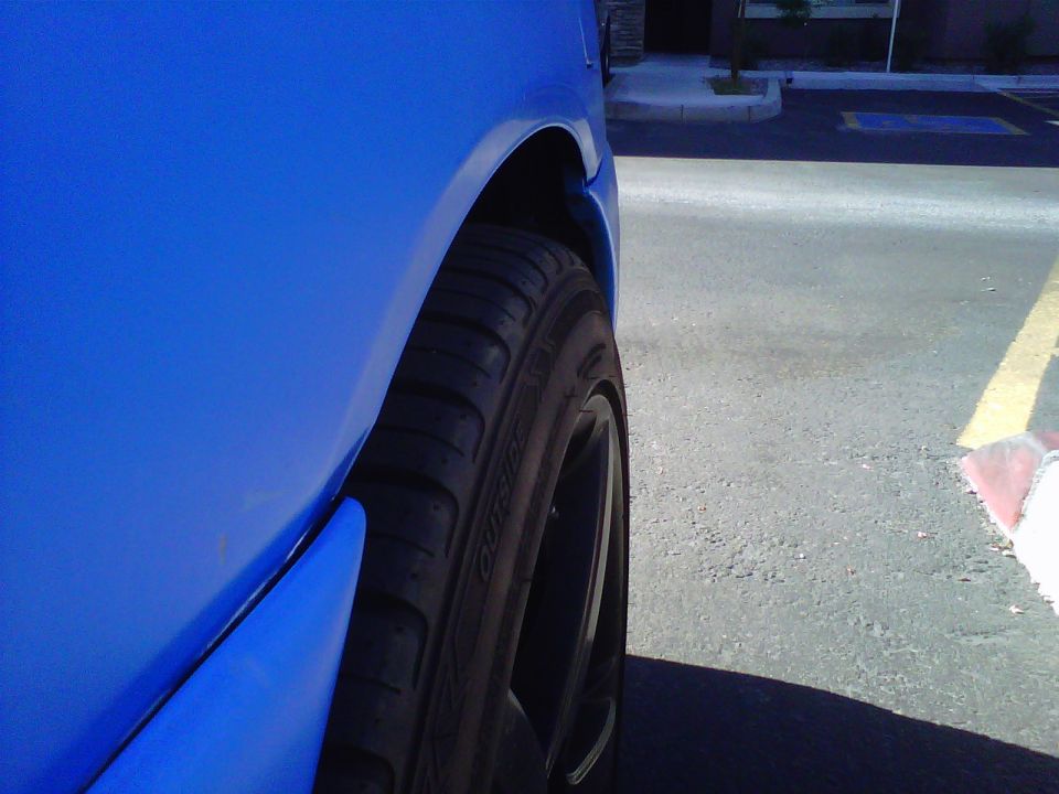Close-up of a blue car's rear wheel and fender. The tire has writing on it