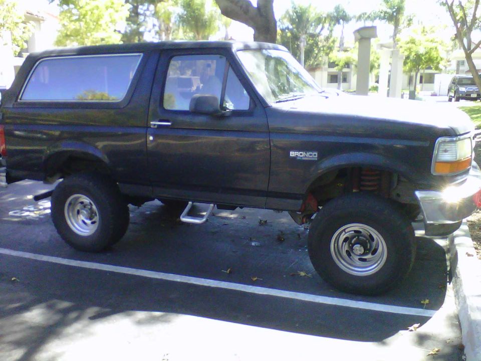 Dark blue Ford Bronco with aftermarket wheels and suspension, seen from the side