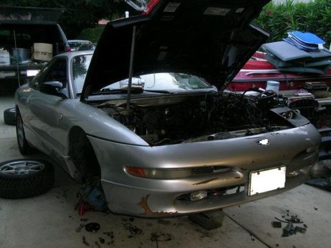 1995 Ford Probe - A silver 1995 Ford Probe is shown with its hood open, revealing the engine bay and some rust on the front bumper.